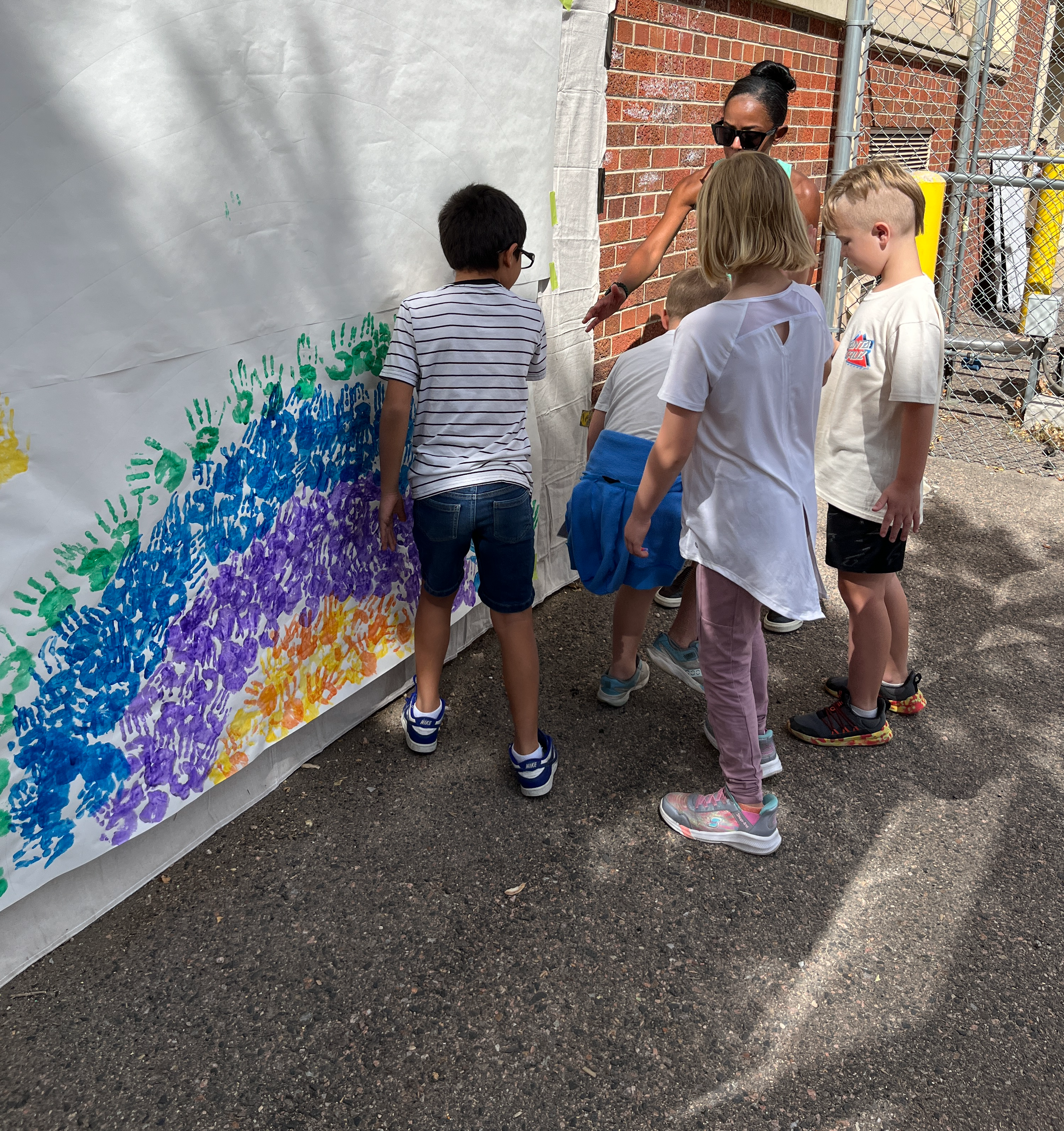 Adult helping students make rainbow with painted handprints