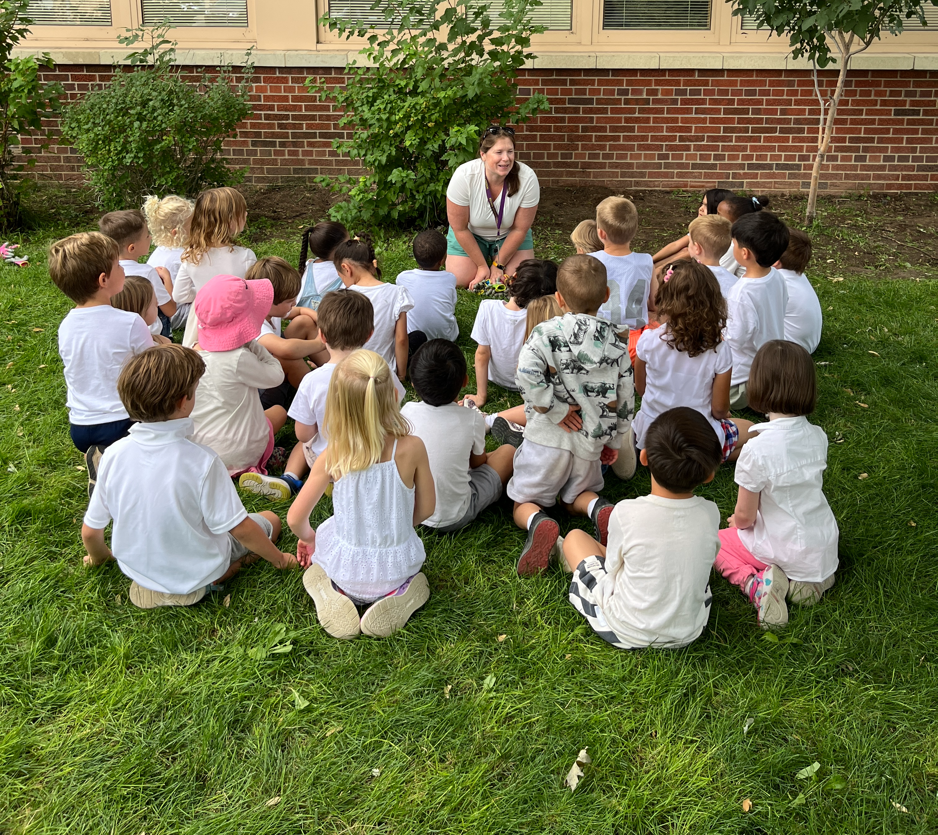 Teacher talking to a class on the lawn in front of the school