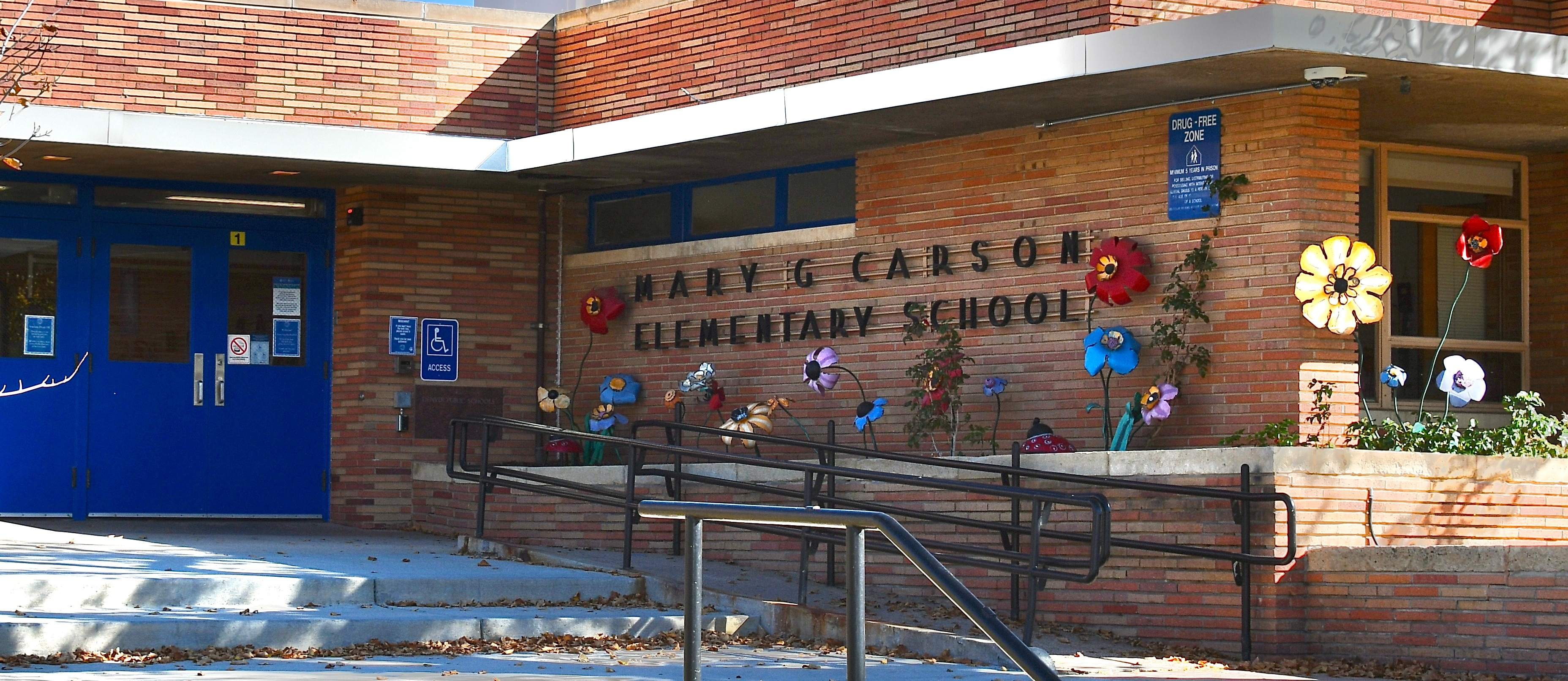 Exterior of a school with brick walls and blue doors. A welcome sign is in front. Steps lead to the entrance.