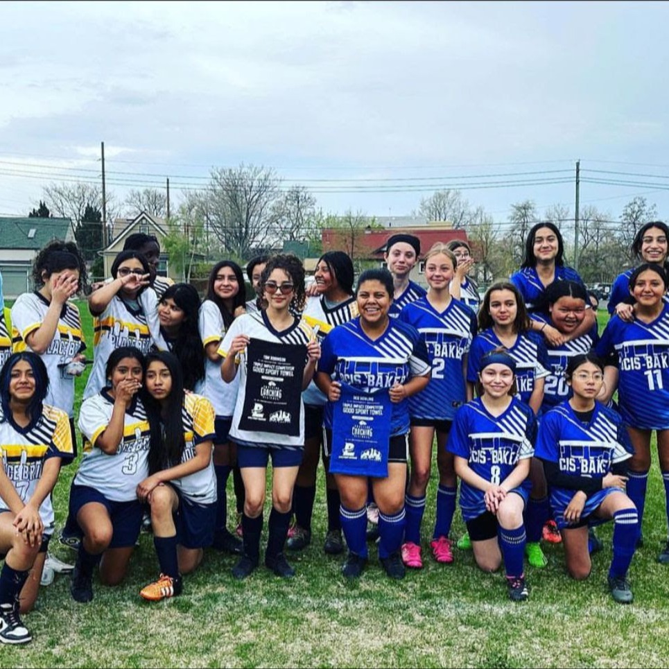 A group of young women wearing blue uniforms pose with a trophy in a grassy area.