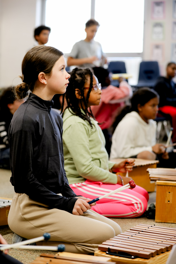 A young girl engrossed in her musical journey, sitting at the drums during an orchestra class.