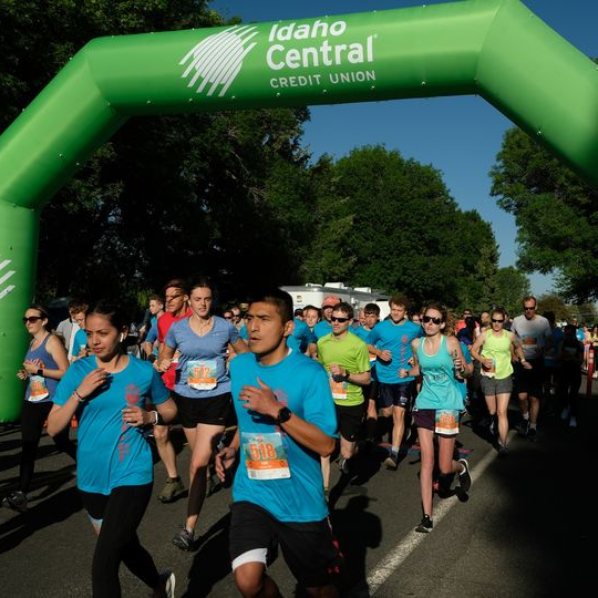 Lots of runners starting a race under the green Idaho Central Credit Union blow-up START arch over the street