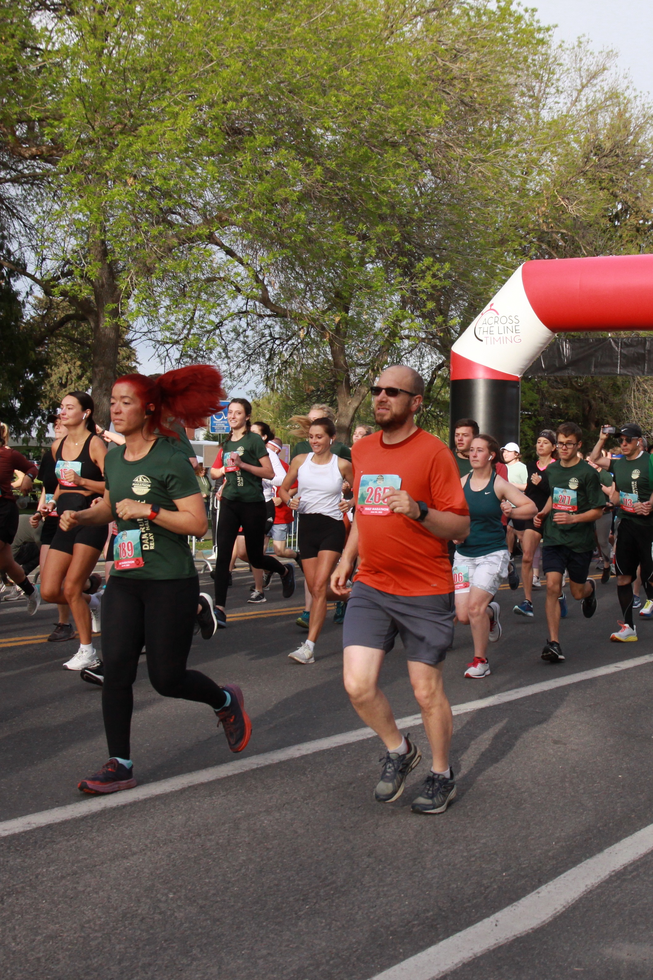 A group of people in various athletic attire run in a marathon, passing a finish arch.