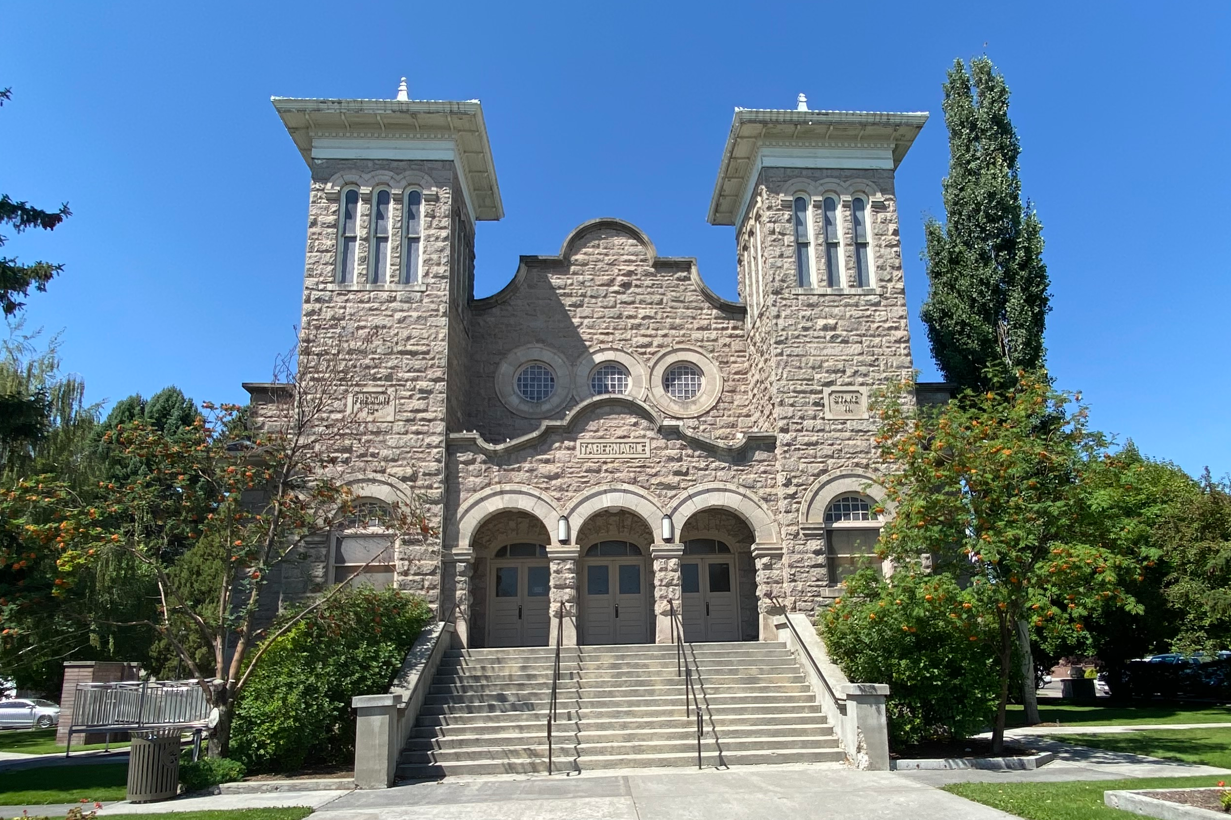 Photo of the tabernacle building from the front in the summer with clear blue sky and green trees surrounding it. 