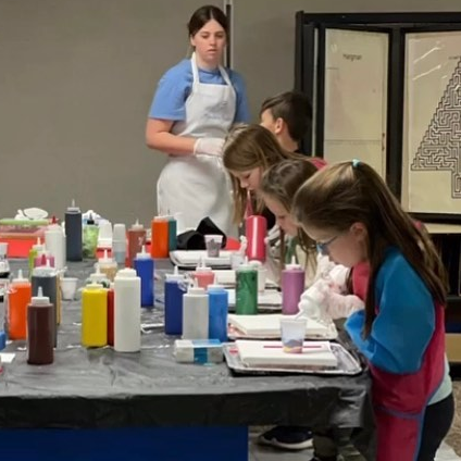 Kids working on an art project at one big table with an adult supervising and leading the class