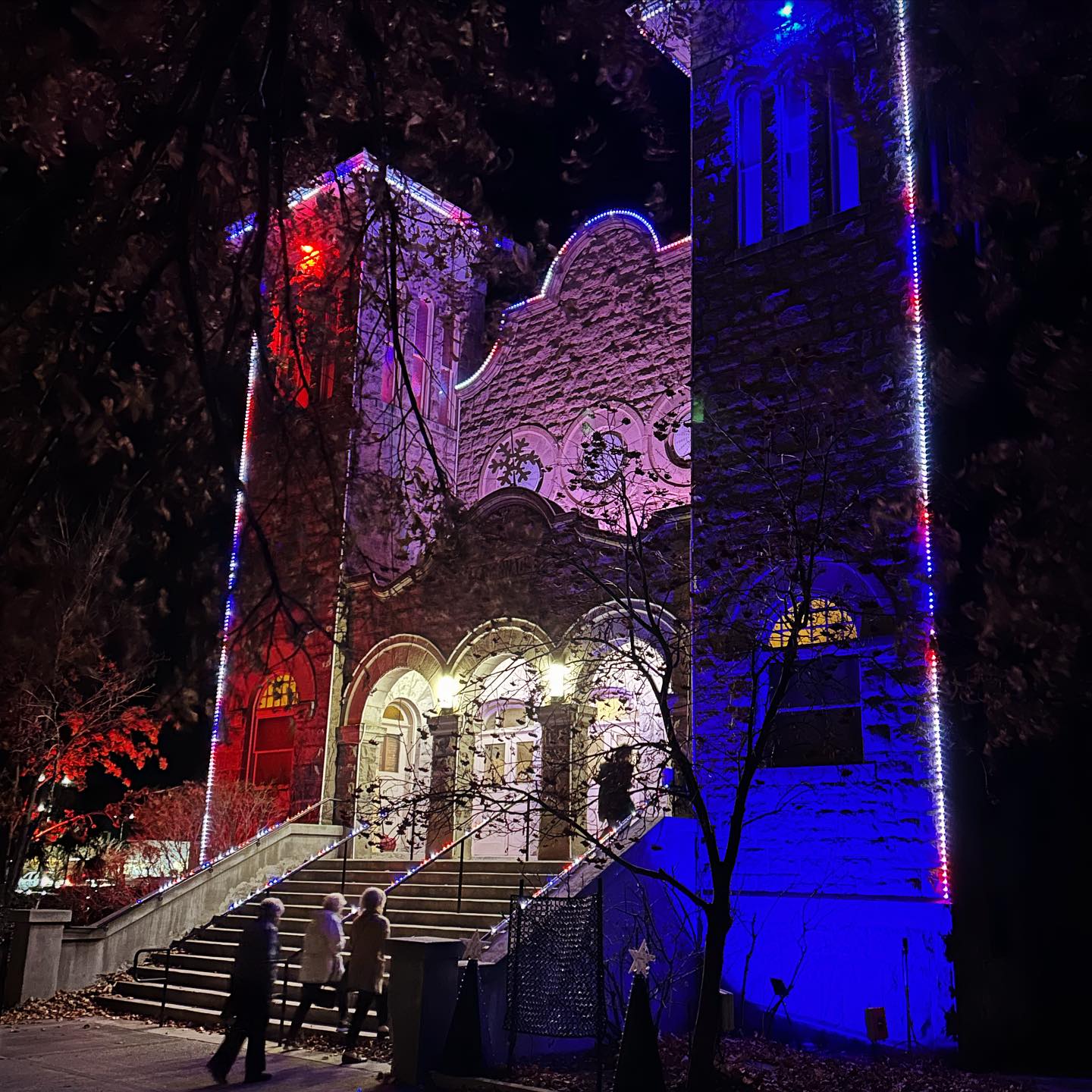 front of the Tabernacle in the winter from an angle, christmas lights on the building make it glow in the night and it is snowing.