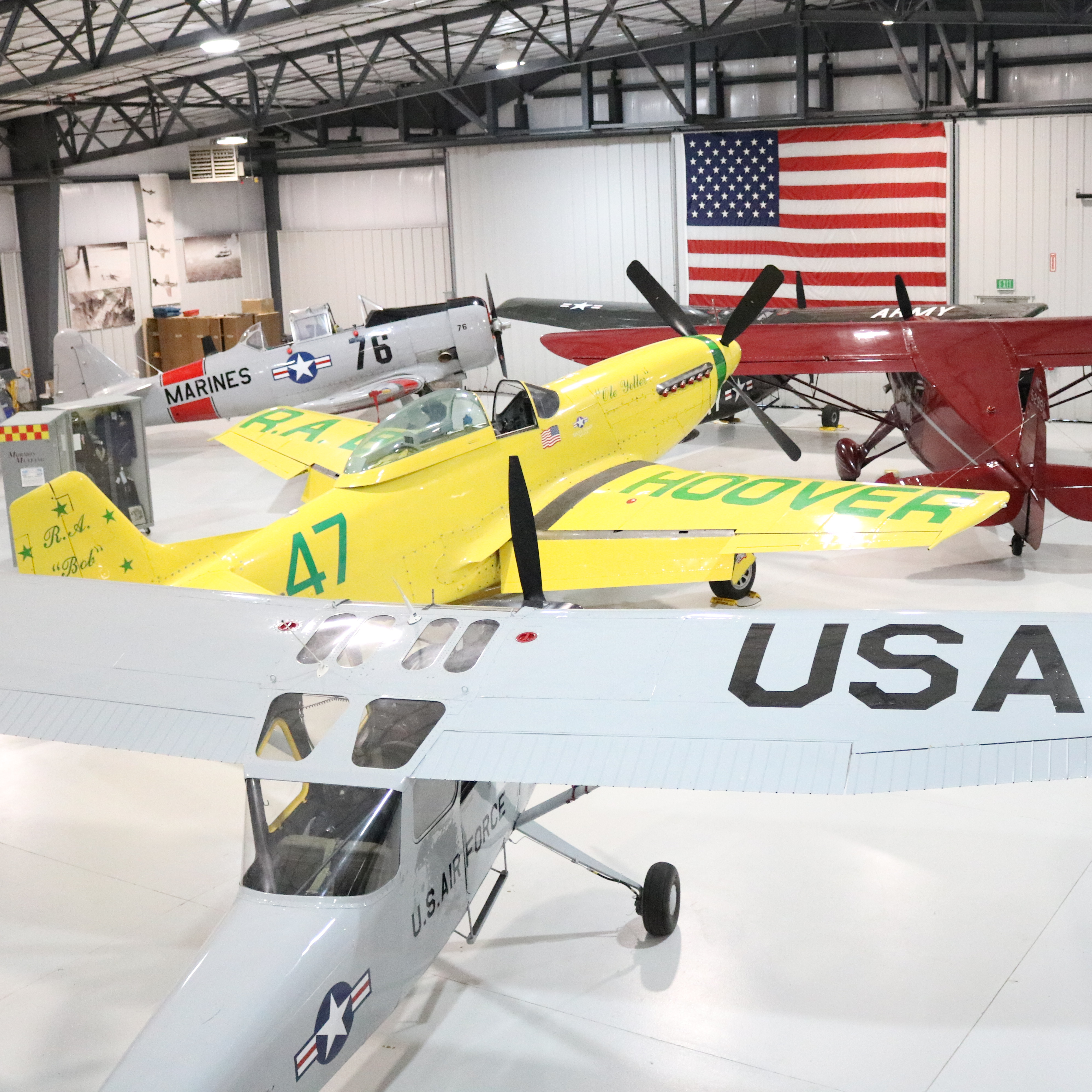 Image of 4 airplanes parked in the hanger that is the Legacy Flight Museum. American Flag on the wall in the background. 