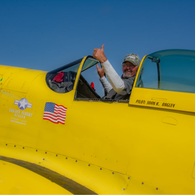 Pilot of a yellow airplane gives a thumbs up from the open cockpit