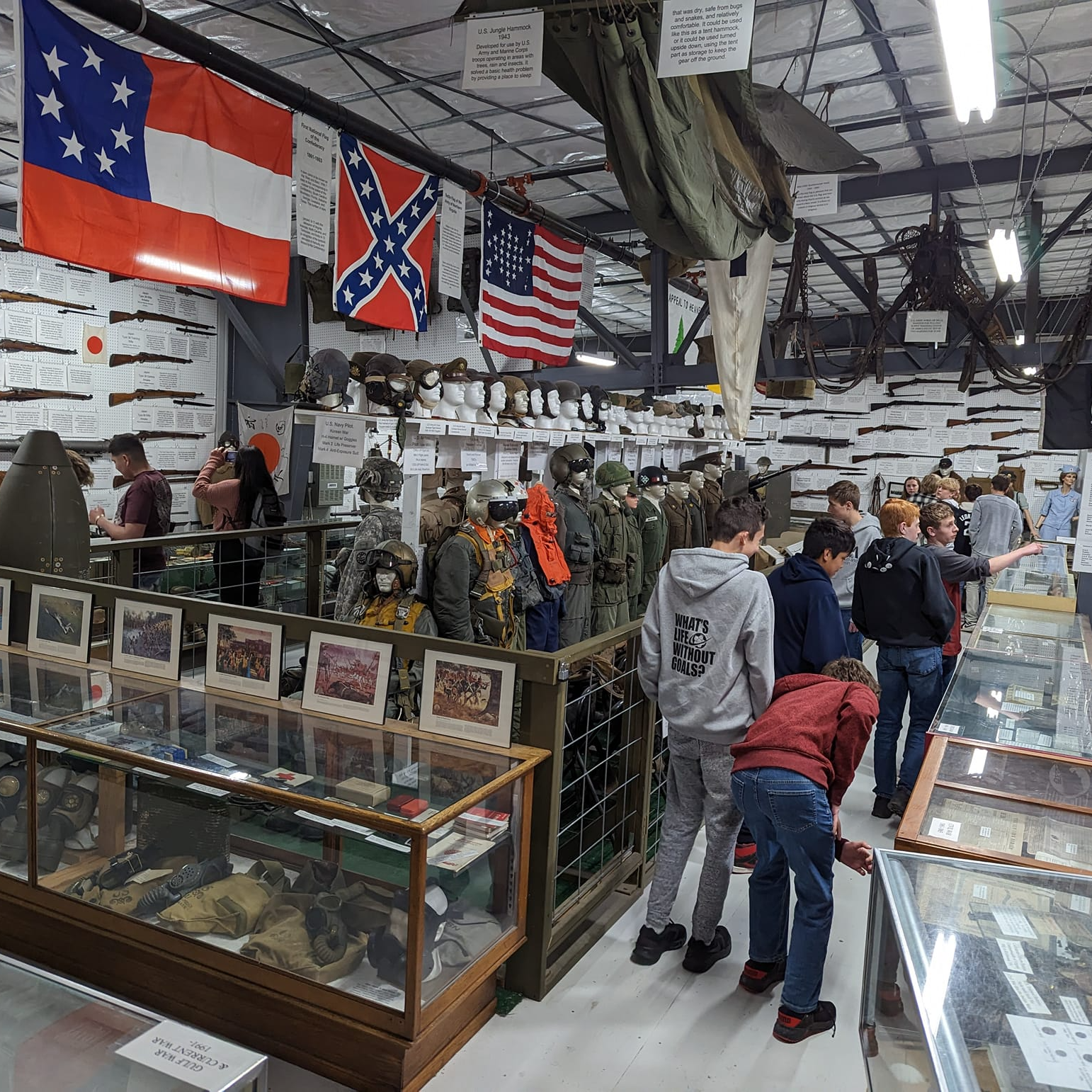 Teens explore the second floor of the museum with military flags, uniforms, and gear - some in enclosed glass cabinets.