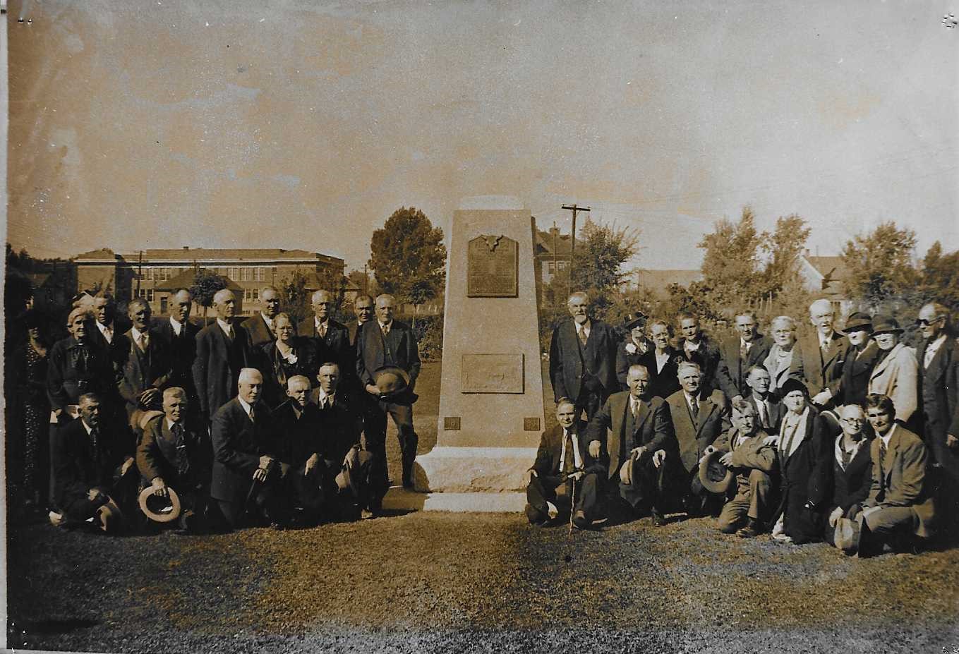 Old sepia photo of a group of men in suits outside one of the monuments at the Tabernacle. 