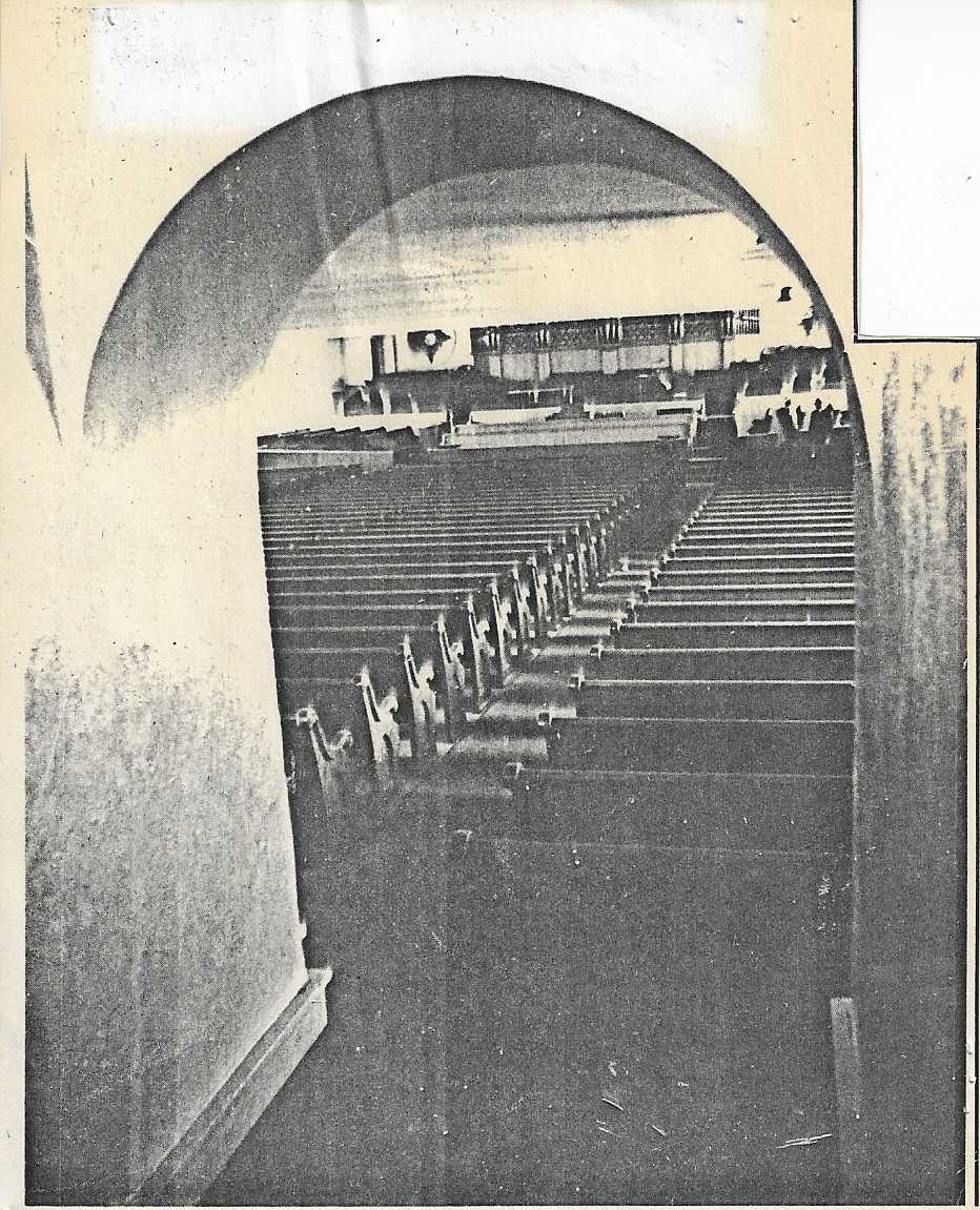 Old sepia photo of the interior of the Tabernacle looking thru an arch at the backs of the pews and the stage/altar in the back of the image.