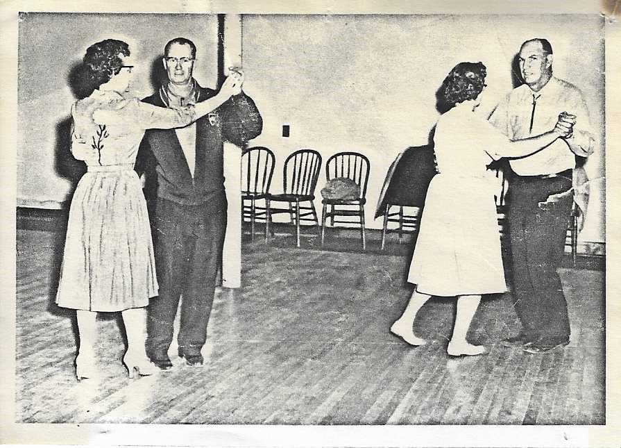 Old B&W photo of two couples dancing on the hardwood floor. 