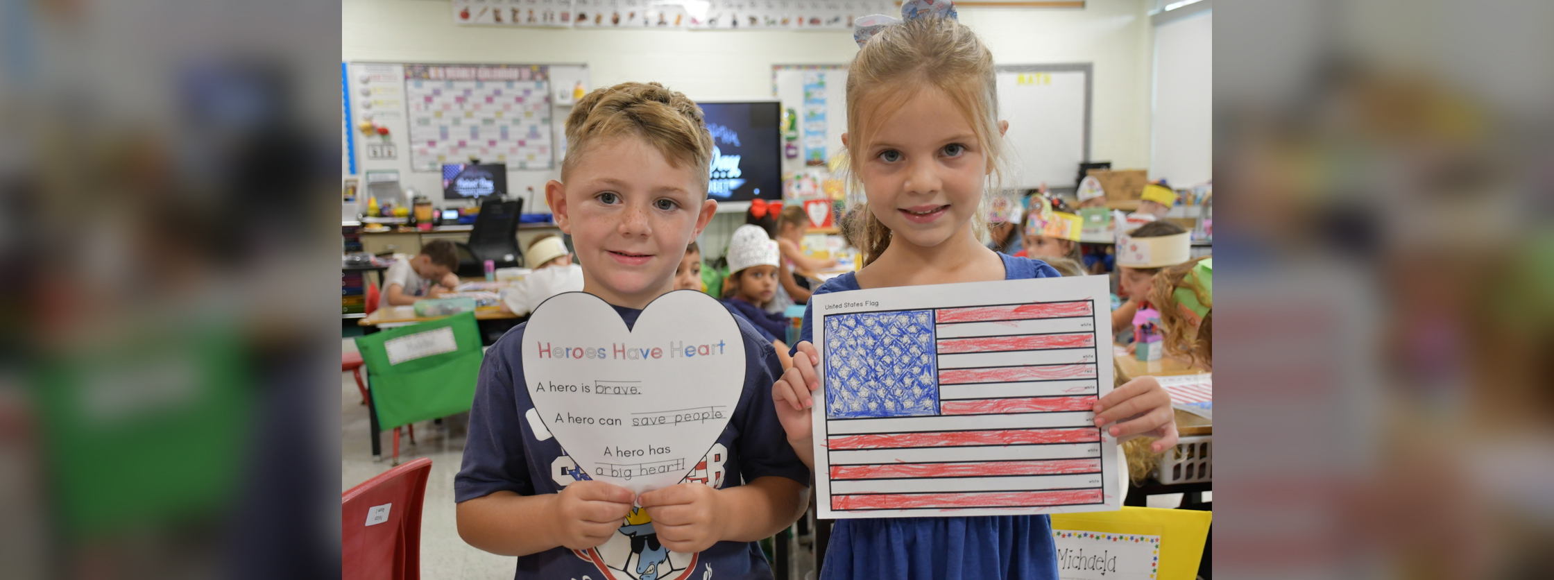 Two people hold artwork, one featuring a heart and the other the United States flag.