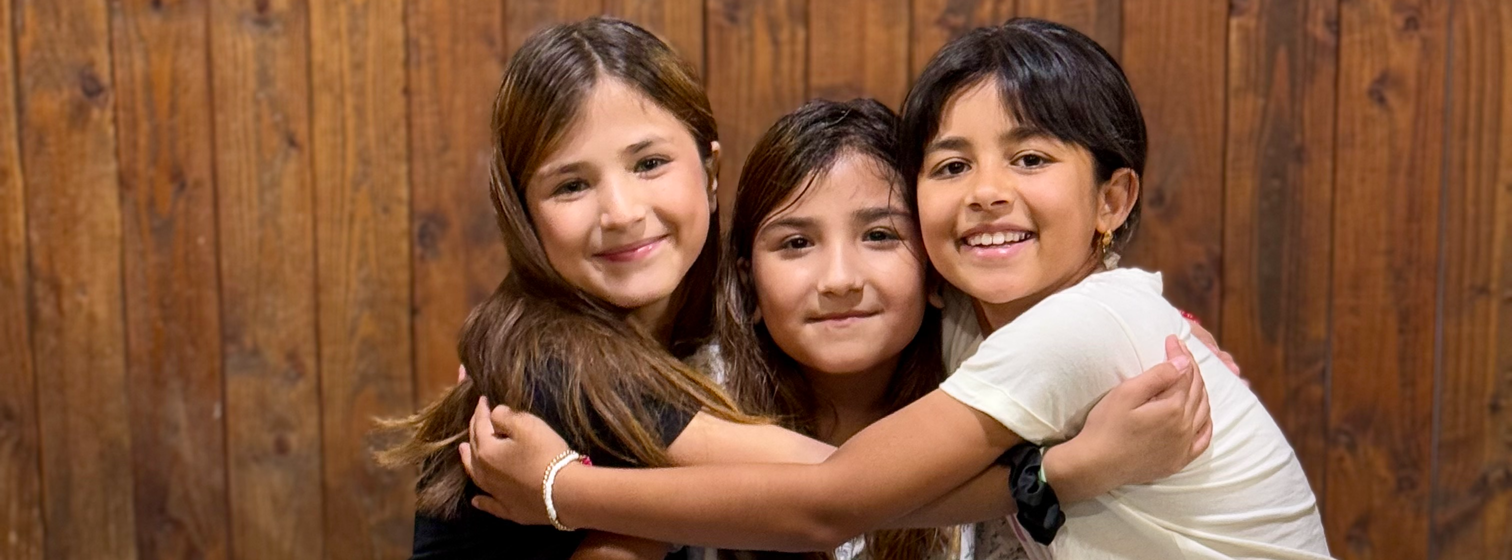 three students hugging each other sitting on floor smiling at the camera