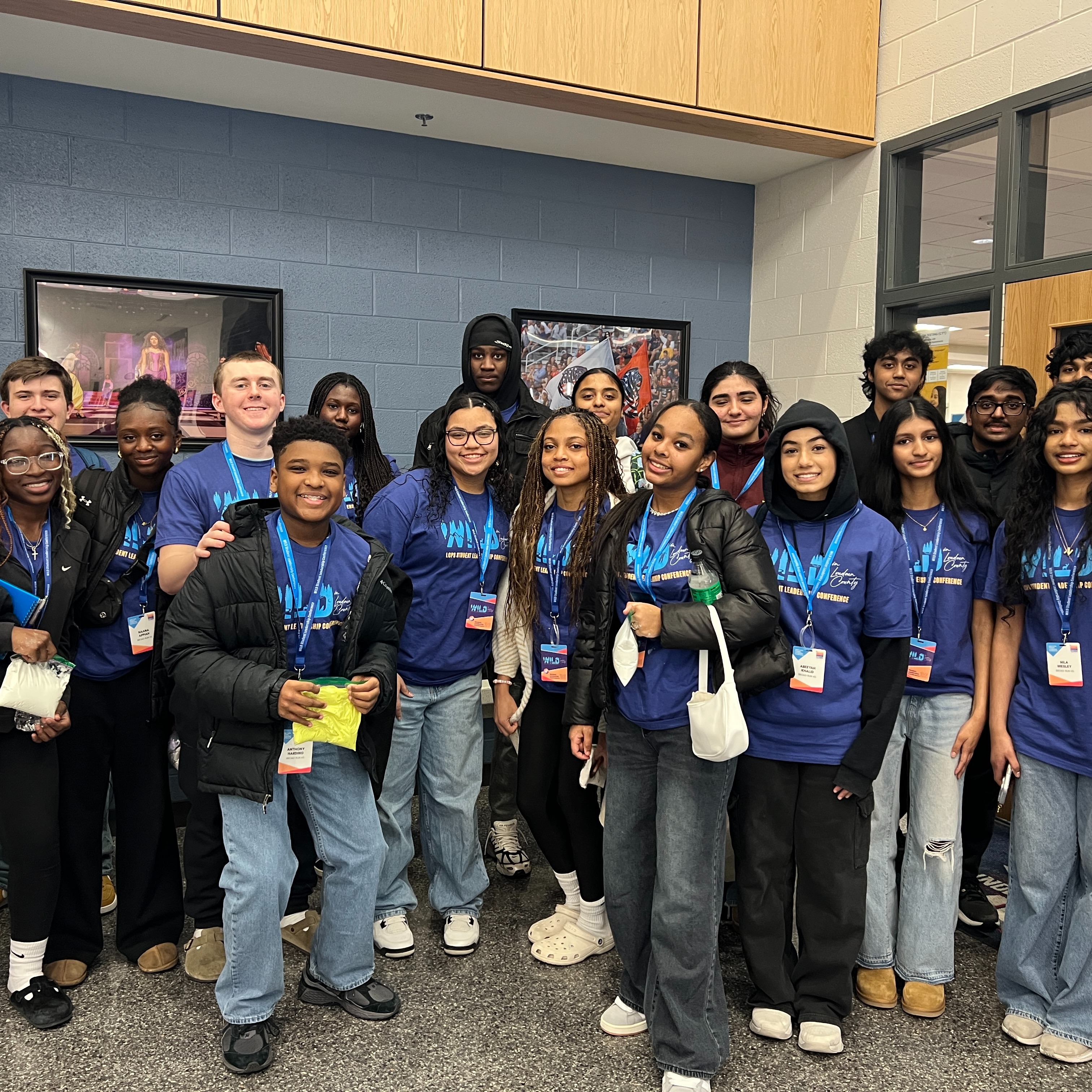 A group of students in blue shirts pose for a photo in a room with blue walls.