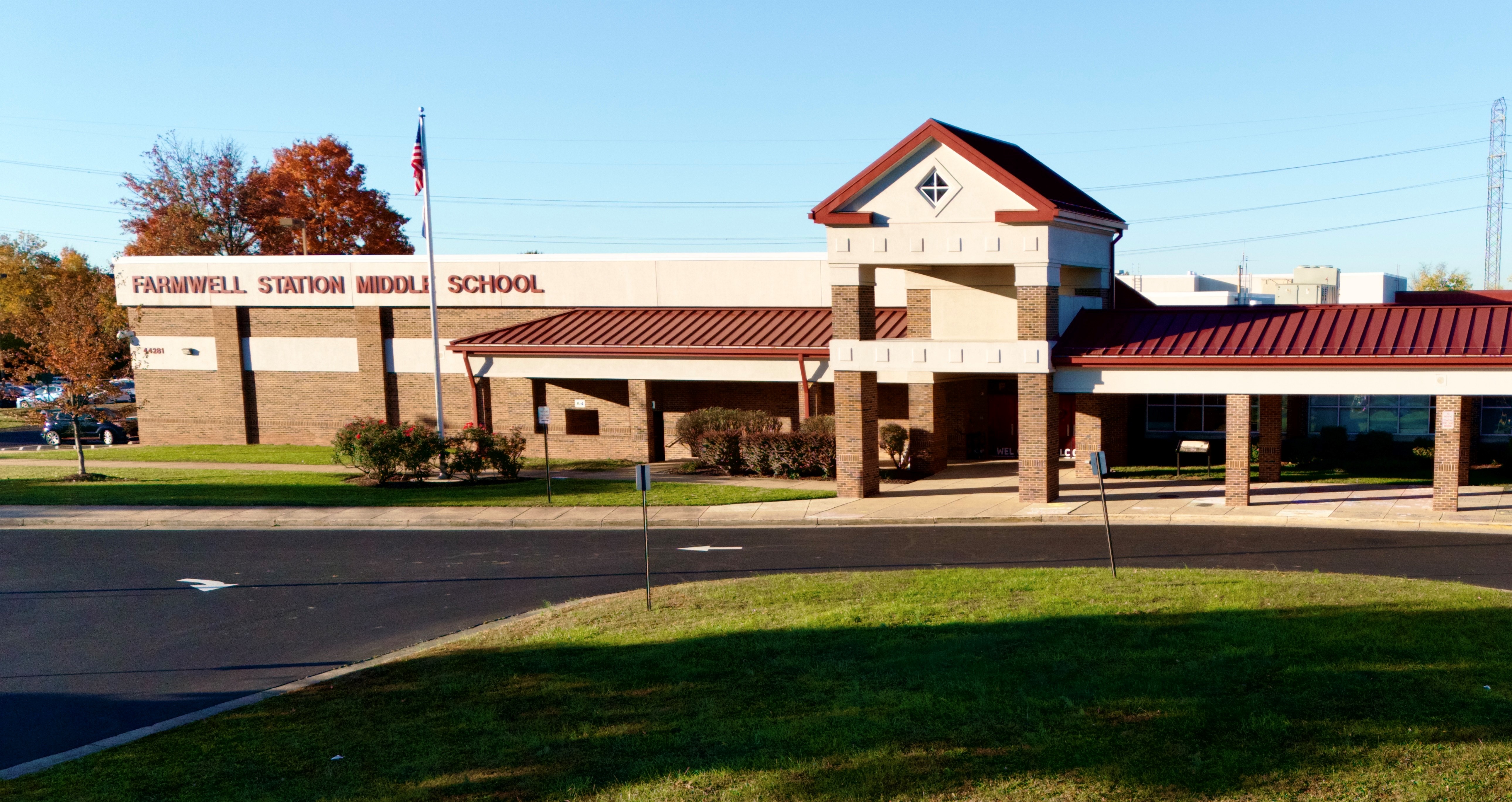 Front of a school with red roof, a flag, and a lawn in front. Trees in the background.