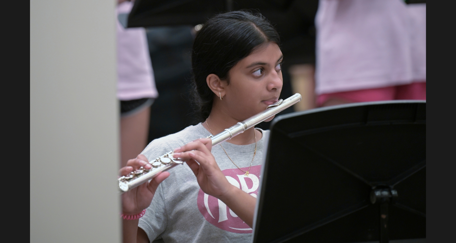 A girl plays a flute while standing, with music notes on a black stand in front of her.