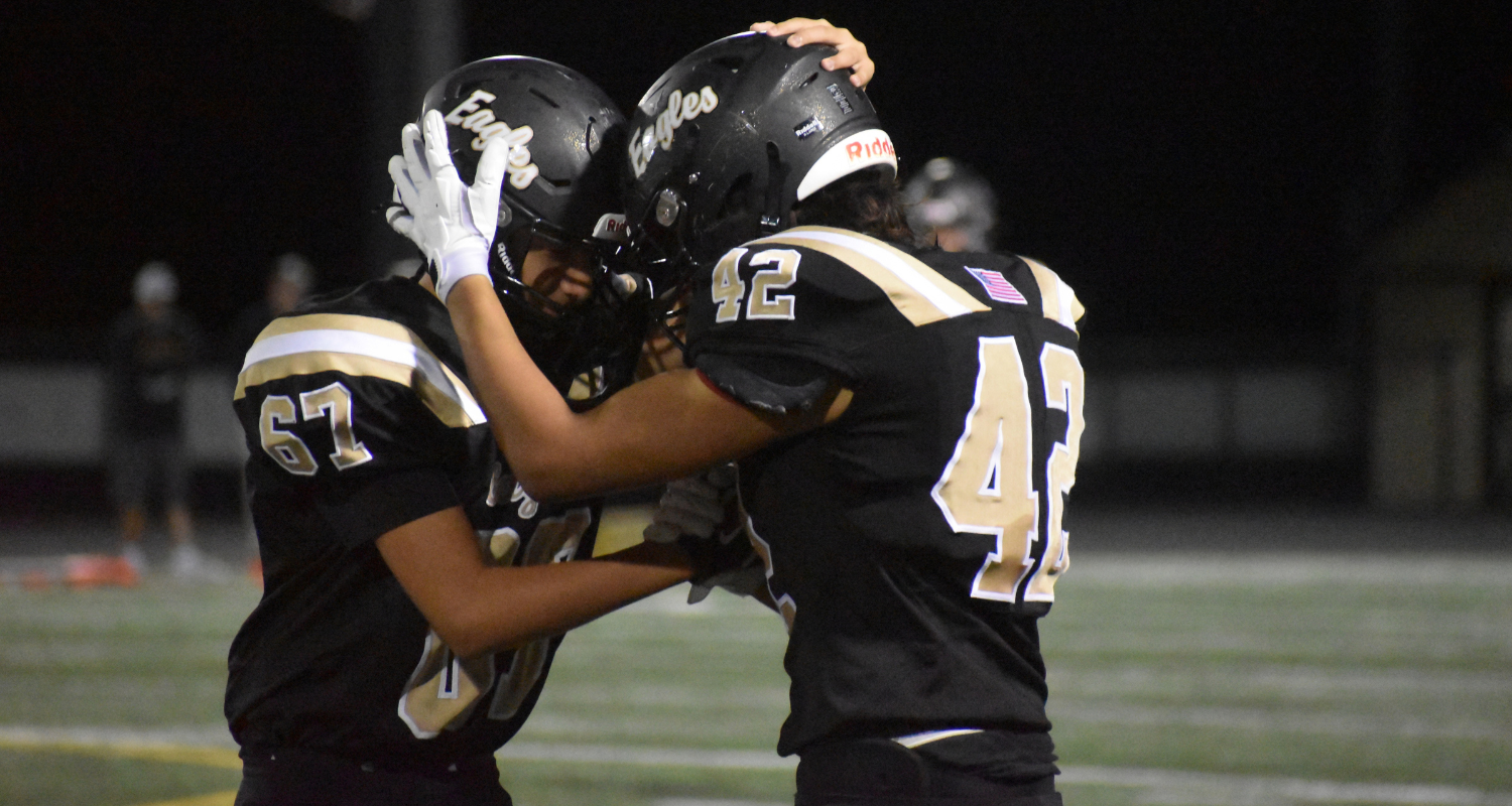 Two football players, jerseys numbered 57 and 42, embrace on a field at night.
