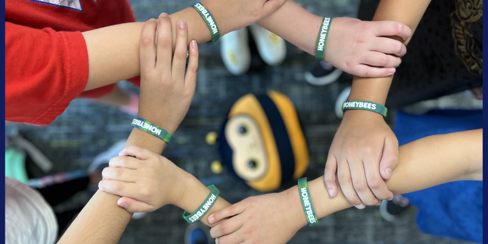 6 students holding arms together to form a circle, all wearing honeybee bracelets