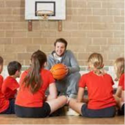 male coach in grey teaching small children about basketball in a circle 