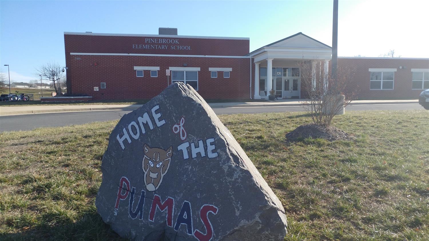 A large rock with "Home of the Pumas" written in red in front of a red building.