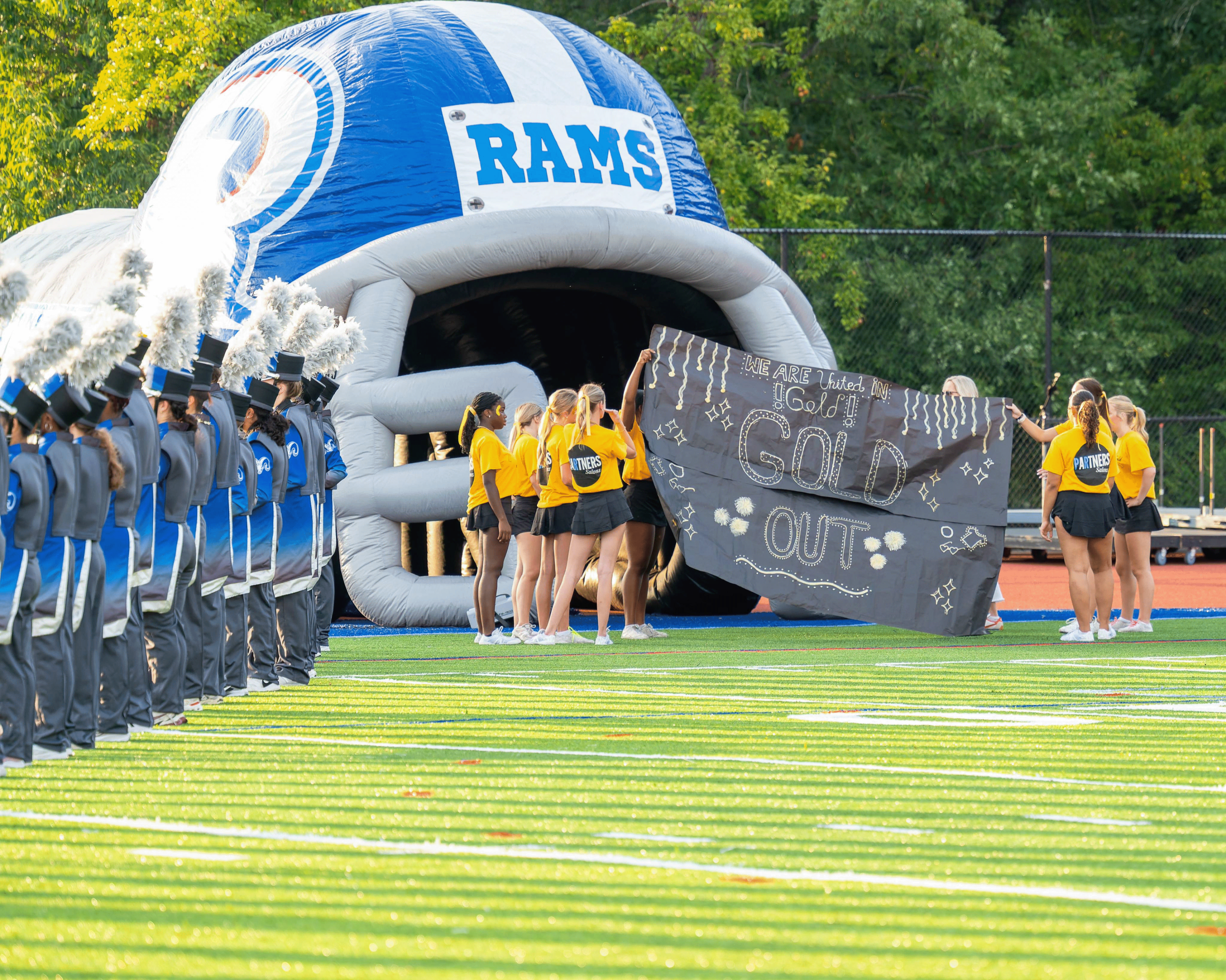 Cheerleaders with blue and white uniforms holding a sign that reads "GO OUT" in front of a large inflatable helmet.