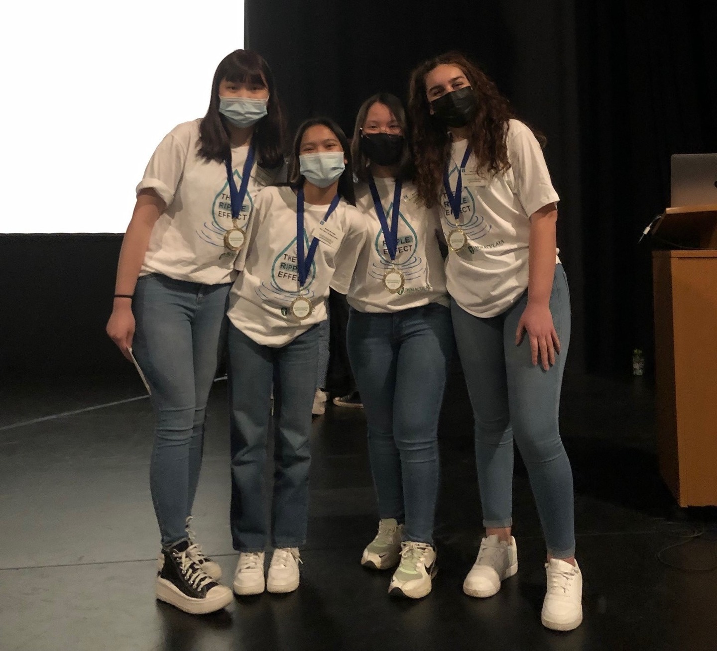 four students after giving a presentation, smiling at the camera, using masks each