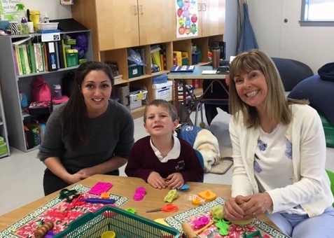 two teachers and a little kid student in the classrom smiling at the camera