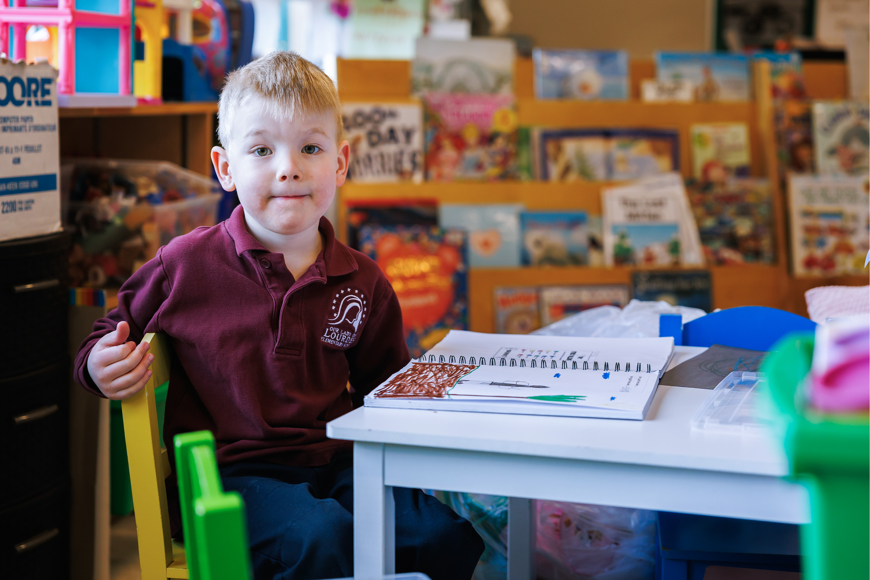 Boy with workbook on desk and reading books behind him