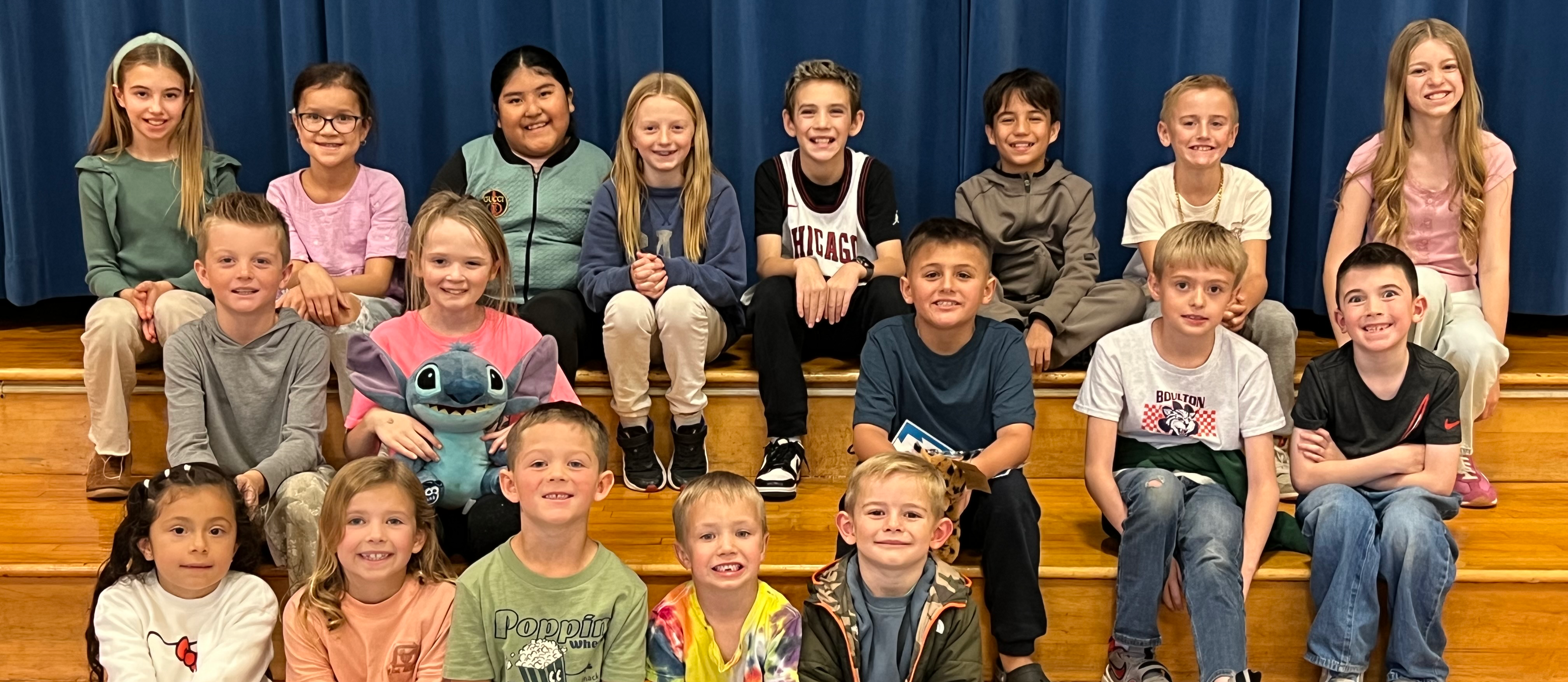 Students sitting on stage steps holding Bobcat award.
