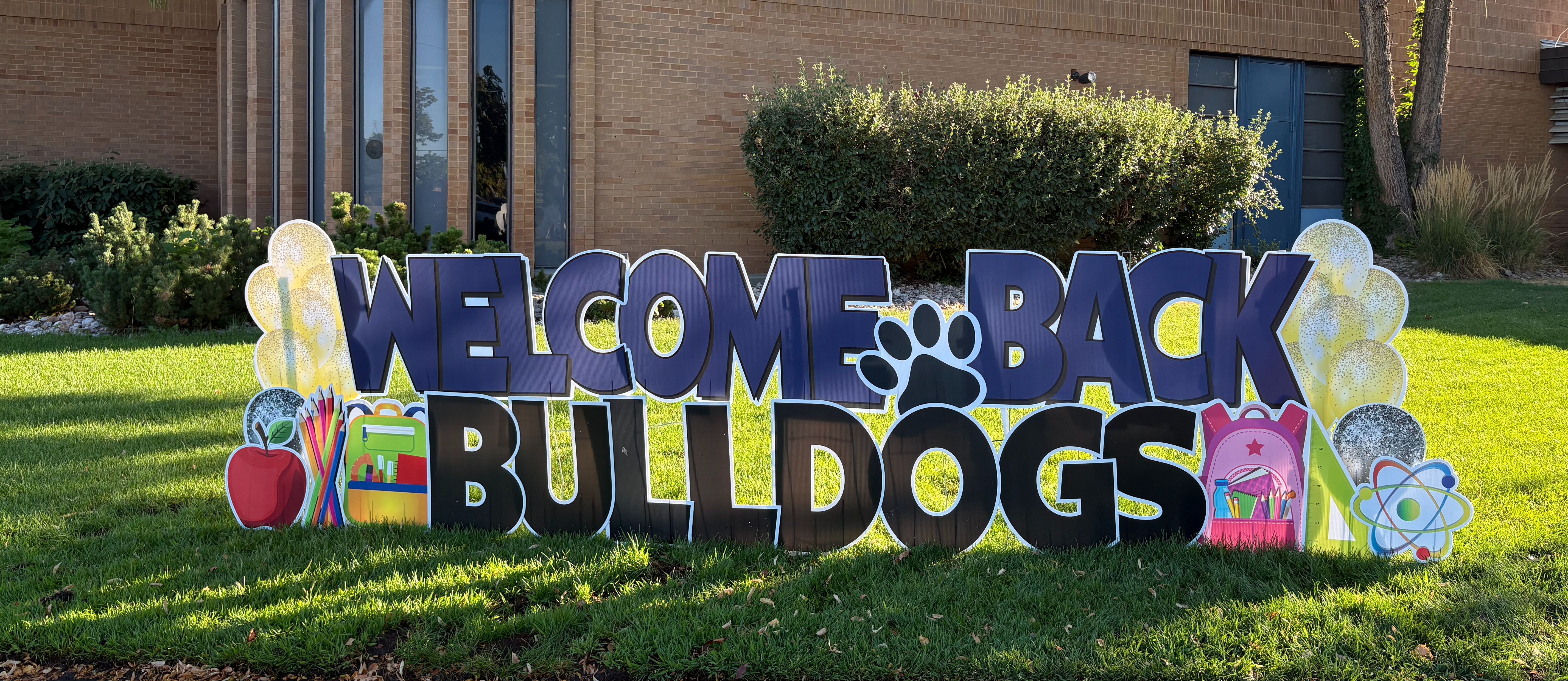 A big sign in the grass in front of the school that says, "Welcome Back Bulldogs"