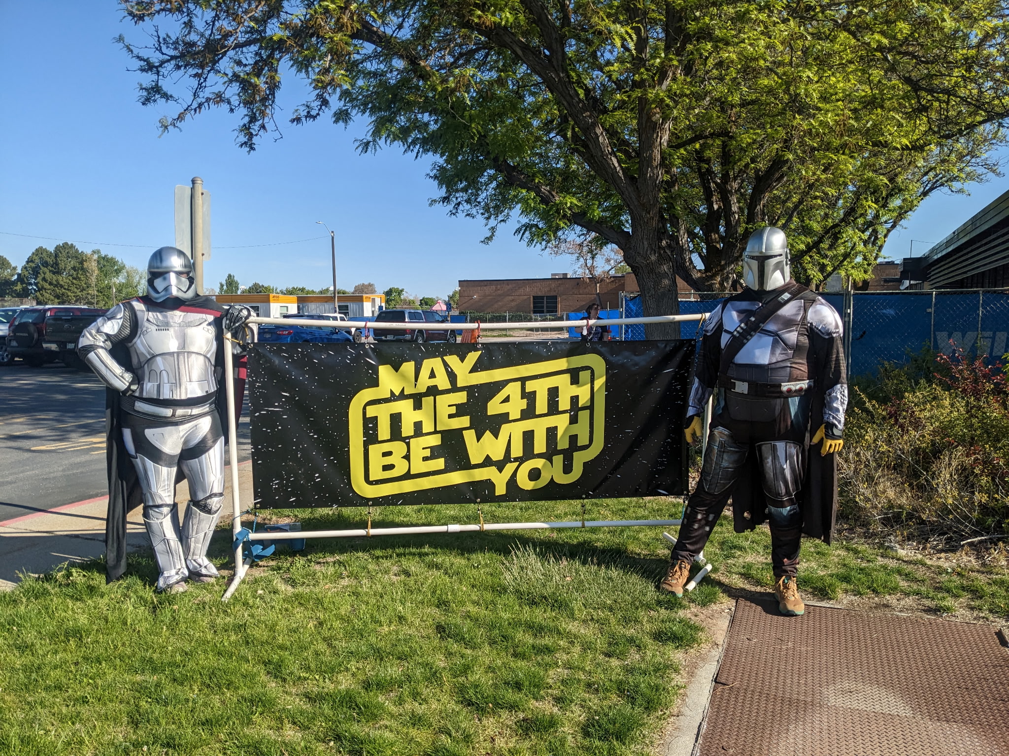 Two people dressed as star wars characters with a sign that says, "May the 4th be with you."