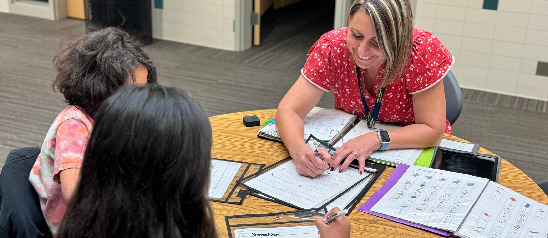 An educator works with two students at a small-group table, using instructional materials and guided practice to support learning and skill development in the classroom.