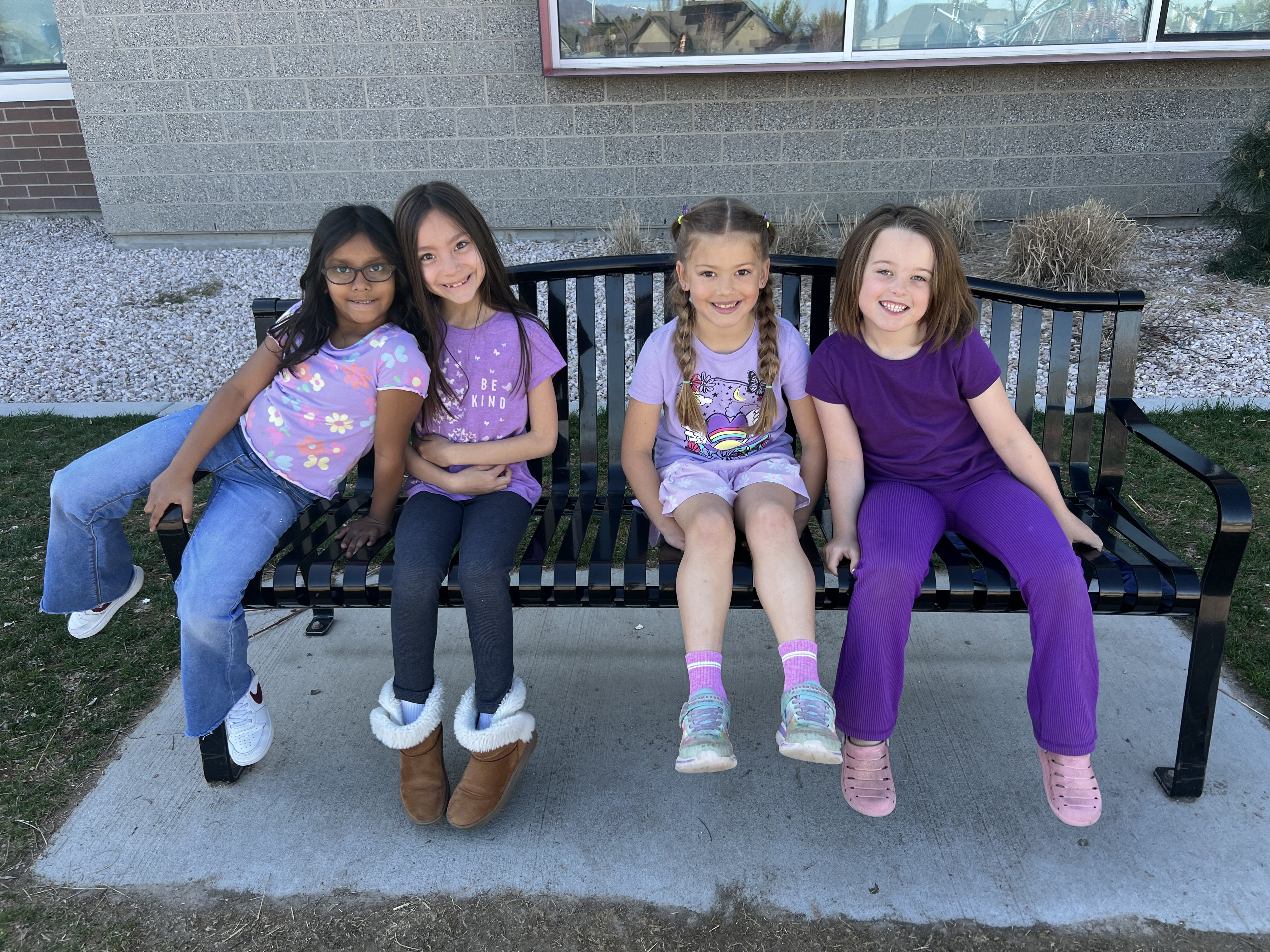 4 students wearing purple and sitting on a school bench.