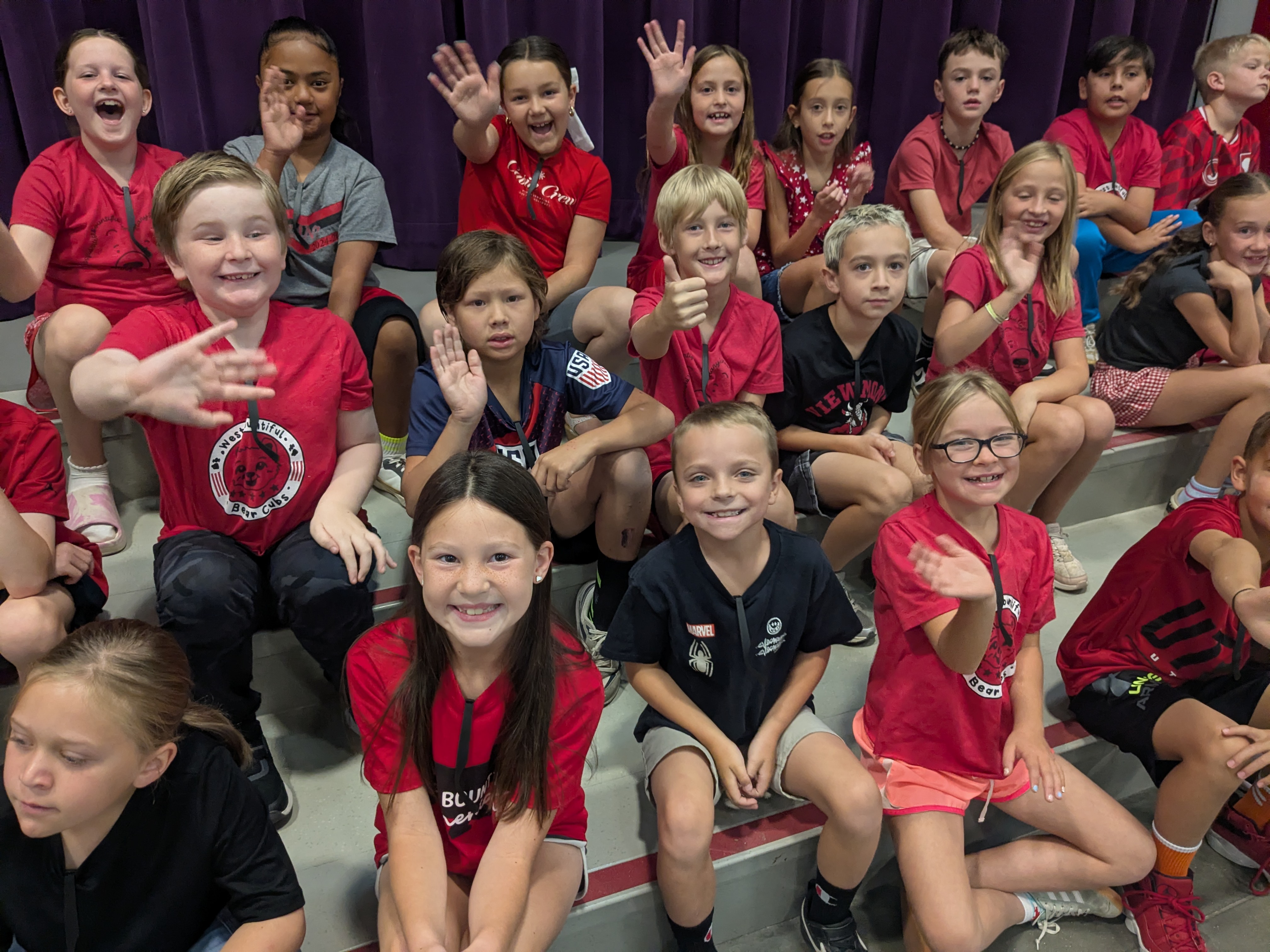 Third grade students wearing red and black sitting on the stage for their performance.