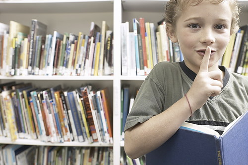 A young boy holds a book in front of him, engrossed in its contents, displaying curiosity and a love for reading.