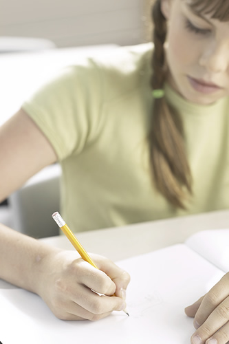 A young girl focused on writing on a piece of paper with a pen in her hand.
