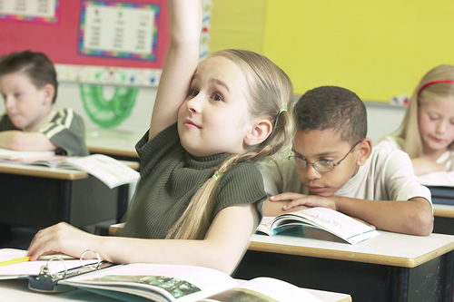 A young girl eagerly participating in class by raising her hand to ask or answer a question.