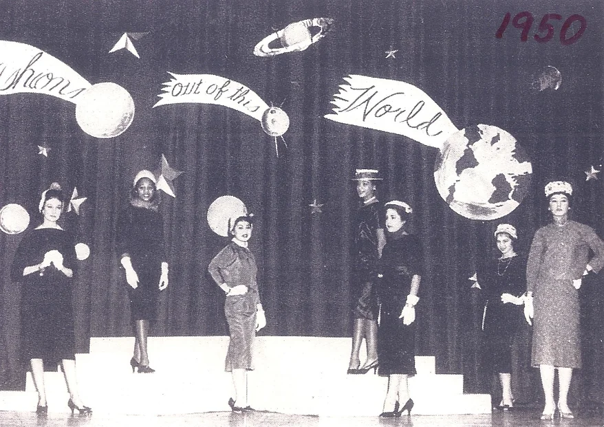 black and white 1950s photo of five women standing onstage posing in fashionable clothes and hats
