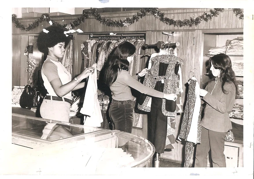 black and white 1970s photo of three young adults or teenagers looking at clothes in a store