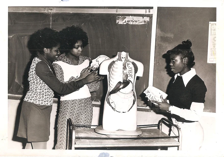black and white 1970s photo of three high school girls of color inspecting a anatomically correct model of a torso