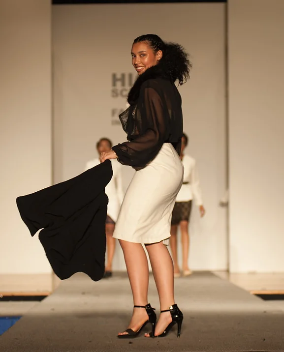 2000s photo of a model turning at the end of a runway wearing a sheer black shirt and white pencil skirt