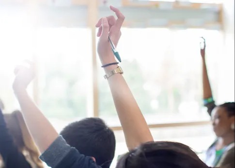 teenage students raising their hands in a classroom