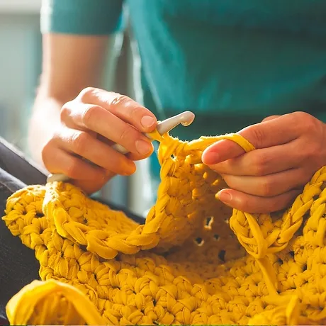 close up of hands crocheting yellow yarn