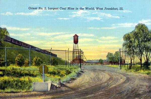 A vintage postcard featuring a picturesque small-town scene with a water tower, power lines, and a dirt road leading to a bridge.