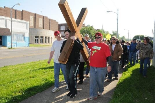 A group of people holding a large wooden cross and marching down the street, engaging in peaceful protest.