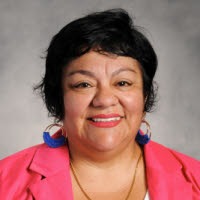 a woman with blue earrings and wearing pink blazer