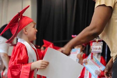 A young boy in a graduation gown receiving his diploma from a woman.