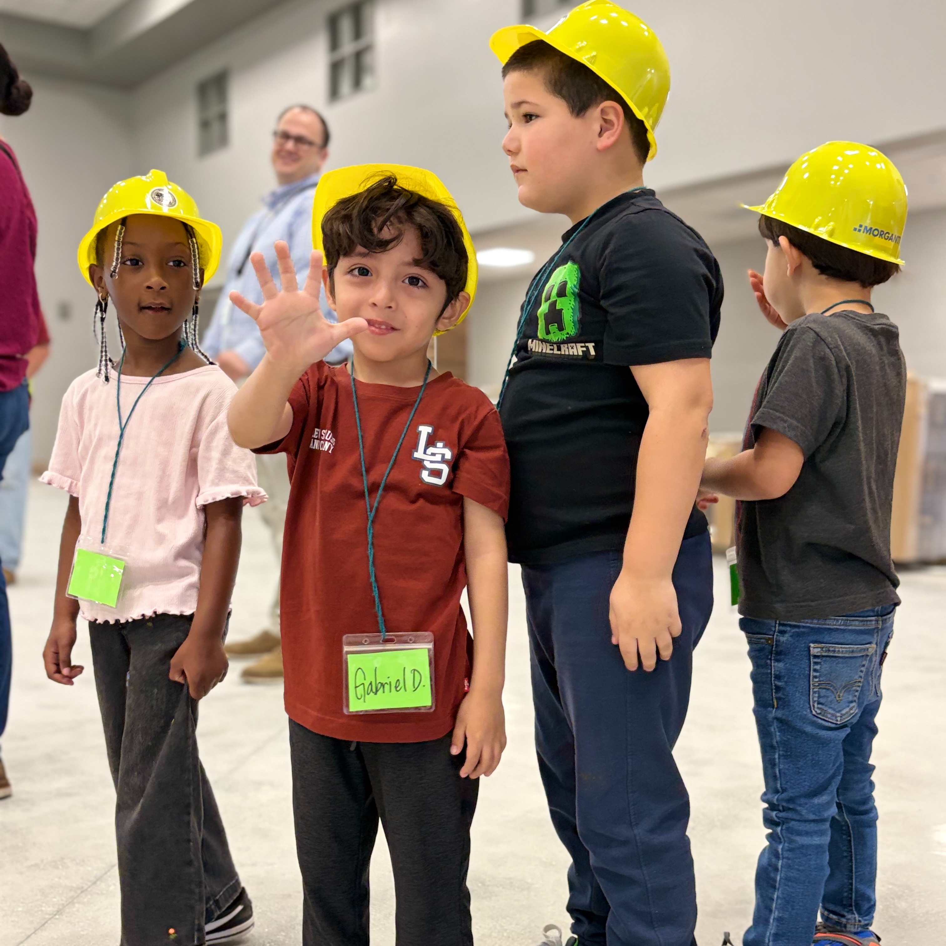 Four children, one wearing a green name tag, are standing next to each other in a room.