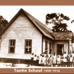 Old black-and-white photo of students standing in front of a one-room schoolhouse.